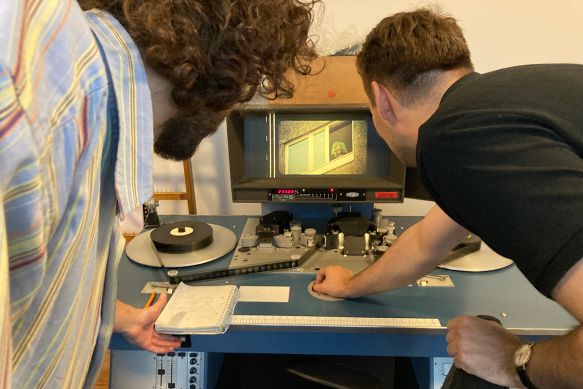Zwei Männer von hinten schauen auf einen Bildschirm, auf dem ein Film mit einem Projektor abgespielt wird.