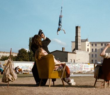 Zwei Frauen sitzen auf Sesseln in einer Berliner Brachlandschaft. Sie schauen auf einen Bungee-Jumper, der am Seil im Himmel h&auml;ngt.