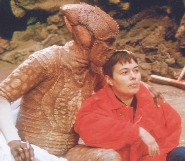 Costume designer Monika Bauert with an actor in a lizard costume on the film set. The actor hugs her and kisses her on the head.