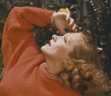 Marlene Dietrich in einem roten Strickpullover schaut in den Himmel.