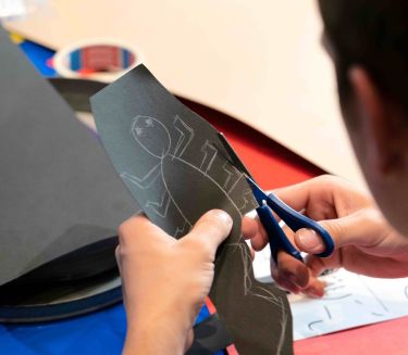 Ein Kind schneidet einen K&auml;fer f&uuml;r einen Trickfilm aus schwarzer Pappe aus.