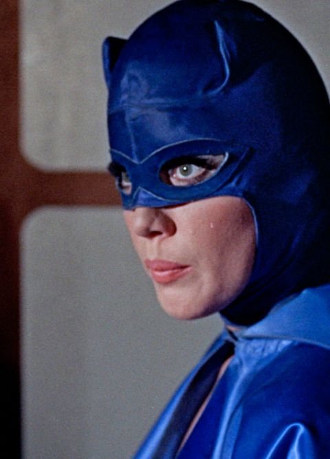 Eine Frau mit langen Wimpern in einer blauen Kost&uuml;mmaske blickt zur Seite.