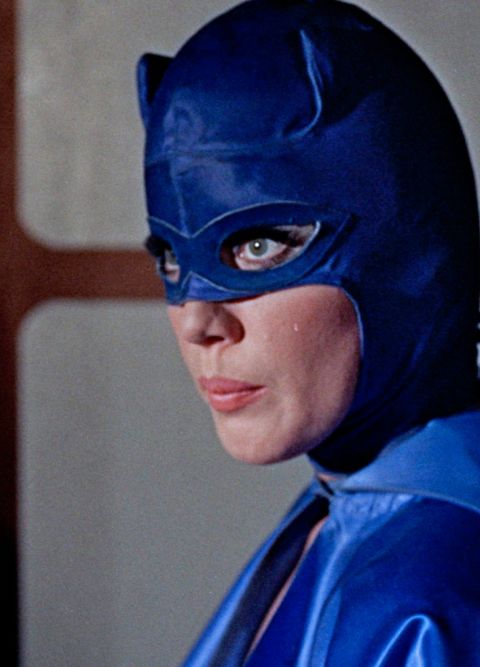 Eine Frau mit langen Wimpern in einer blauen Kostümmaske blickt zur Seite.