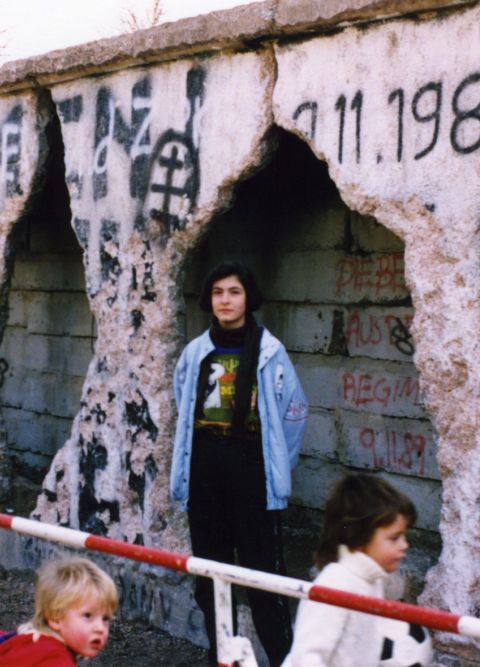 Die Berliner Mauer mit sichtbaren L&ouml;chern und Graffiti, eine Jugendliche und zwei Kinder davor.