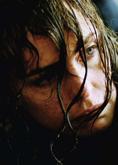 Eine nasse, schmutzige Frau liegt am Boden und schaut hoch.