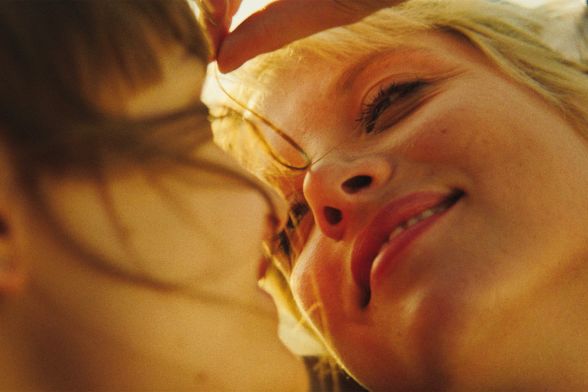 Eine blonde Frau lächelt eine andere Frau in Nahaufnahme an, wobei ihre Gesichter sehr nah beieinander sind.