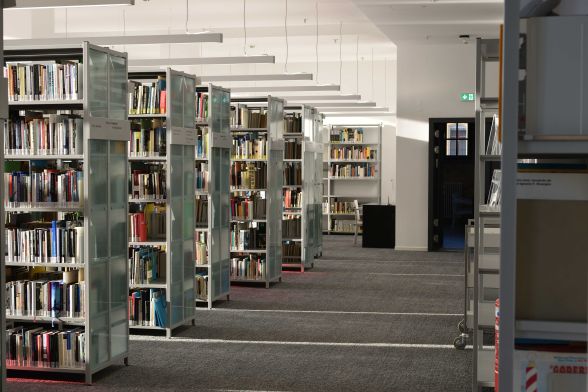 Bücher stehen in Metallregalen in mehreren Gängen mit Durchgang und Fenstern.