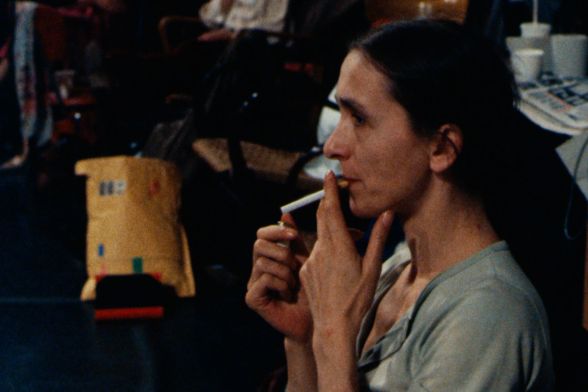 Pina Bausch, a woman with her hair tied in a ponytail, lights a cigarette.