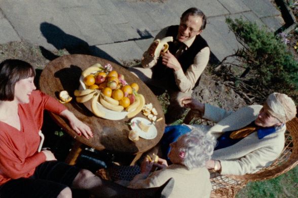 Drei ältere Menschen und eine jüngere Frau sitzen draußen um einen Tisch, auf dem ein großer Obstkorb mit vielen Früchten steht.