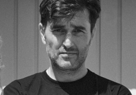 Schwarzwei&szlig;-Portr&auml;t von Mann mit schwarzem T-Shirt, der ernst direkt in die Kamera blickt.