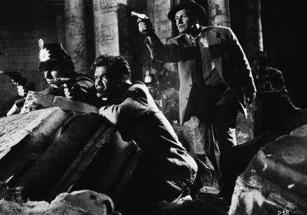 Vier M&auml;nner in Anz&uuml;gen und H&uuml;ten verstecken sich in Tr&uuml;mmern und zielen mit ihren Waffen in dieselbe Richtung.