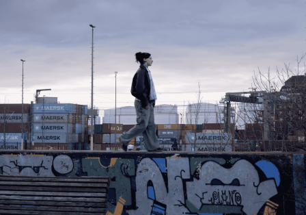Eine Person l&auml;uft in beginnender Dunkelheit auf einer Mauerkante, im Hintergrund Container.
