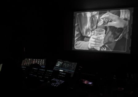 In a dark room, you see a lit-up film clip on a screen; in front of it, sitting in the dark, is someone working.