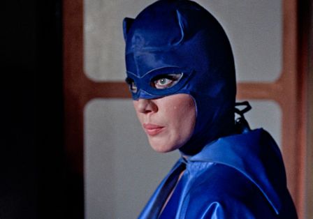 Eine Frau mit langen Wimpern in einer blauen Kostümmaske blickt zur Seite.