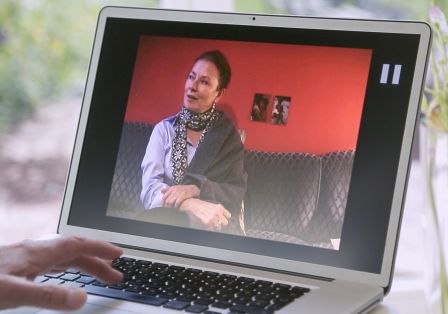 Eine Frau auf einem Laptop-Bildschirm, die mit jemandem spricht, w&auml;hrend sie auf einer Couch sitzt.
