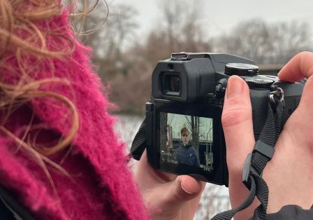 Eine Frauenhand hält eine Digitalkamera, auf deren Display eine Person zu sehen ist.
