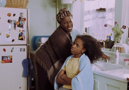 Eine Frau schaut ver&auml;rgert auf ein M&auml;dchen, das genervt vor einem Waschbecken sitzt, mit offenem Haar und einem Handtuch auf den Schultern.