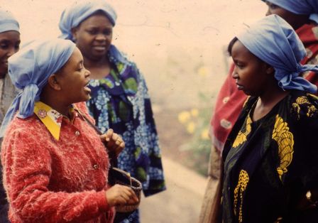 Mehrere Frauen mit blauen Kopft&uuml;chern und farbenfroher Kleidung stehen beisammen, zwei von ihnen wirken in eine Diskussion vertieft.