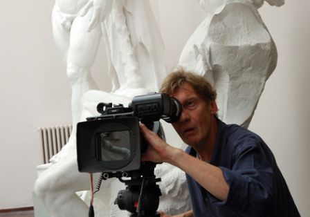 Ein Mann sitzt vor zwei wei&szlig;en Statuen und schaut durch eine Kamera.