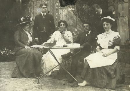 Sechs Mitglieder der Pariser Filmfirma Pathé Frères sitzen fröhlich draußen um einen Tisch.