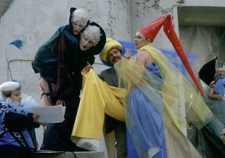 Mehrere Personen in bunten Kostümen stehen vor einem Gebäude und lesen etwas auf einem Blatt.