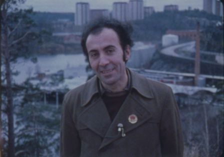 Iranischer Mann mit angestecktem Mikro an der Jacke l&auml;chelt in die Kamera vor einer Stadtansicht.