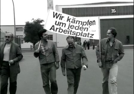 M&auml;nner marschieren mit einem Schild, auf dem steht: Wir k&auml;mpfen um jeden Arbeitsplatz.