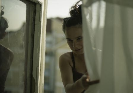Teenager steht im Fenster hinter einer Gardine.