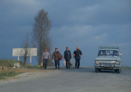 Vier Personen gehen auf einer Stra&szlig;e, ein Auto f&auml;hrt neben ihnen.