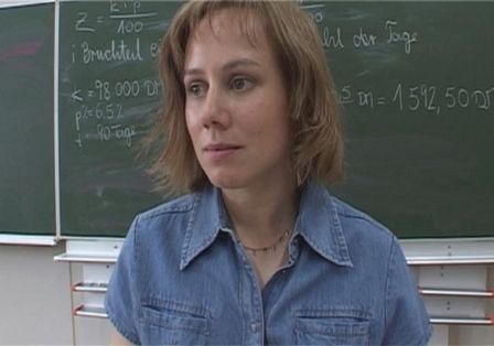 Lehrerin in blauem Hemd vor Tafel.