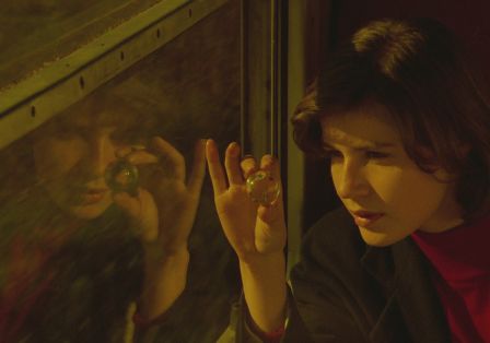 Eine junge Frau sitzt im Zug am Fenster und schat durch eine Glasmurmel. Sie spiegelt sich im Fenster.