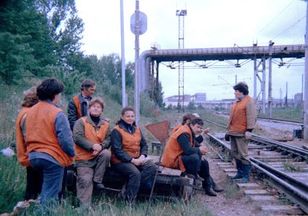Eine Gruppe von Menschen in orangefarbenen Westen steht und sitzt am Rand eines Zuggleises.