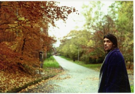 Ein Mann steht auf einem Waldweg und hat sich umgedreht, um in die Kamera zu schauen.