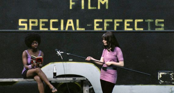 Zwei Frauen bei einer Filmproduktion, eine liest auf einer Bank, die andere h&auml;lt eine Tonangel. Im Hintergrund steht: FILM SPECIAL-EFFECTS. 