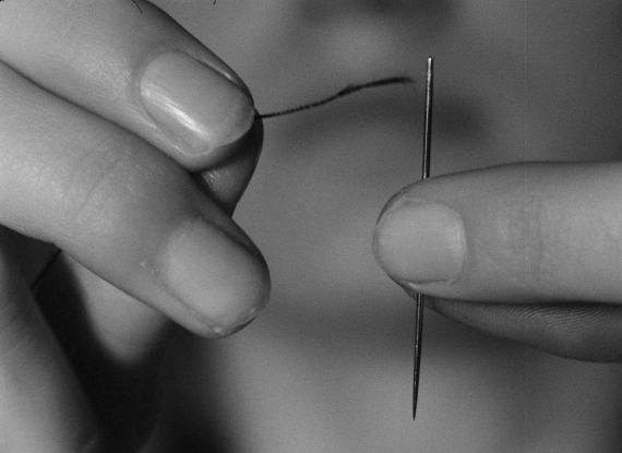 Eine Hand führt einen Faden zu einer Nadel.