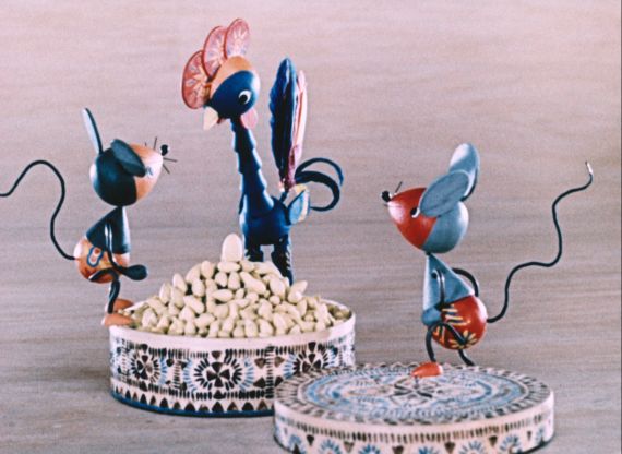 Zwei kleine Holzmäuse und ein Holzhahn stehen um eine Schüssel mit Korn.