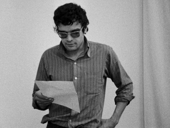 Ein Mann mit getönter Brille hält ein Blatt Papier in der Hand und liest.