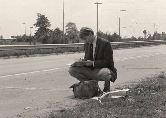 Ein Mann im Anzug sitzt auf einem Straßenrand und schreibt in ein Buch.