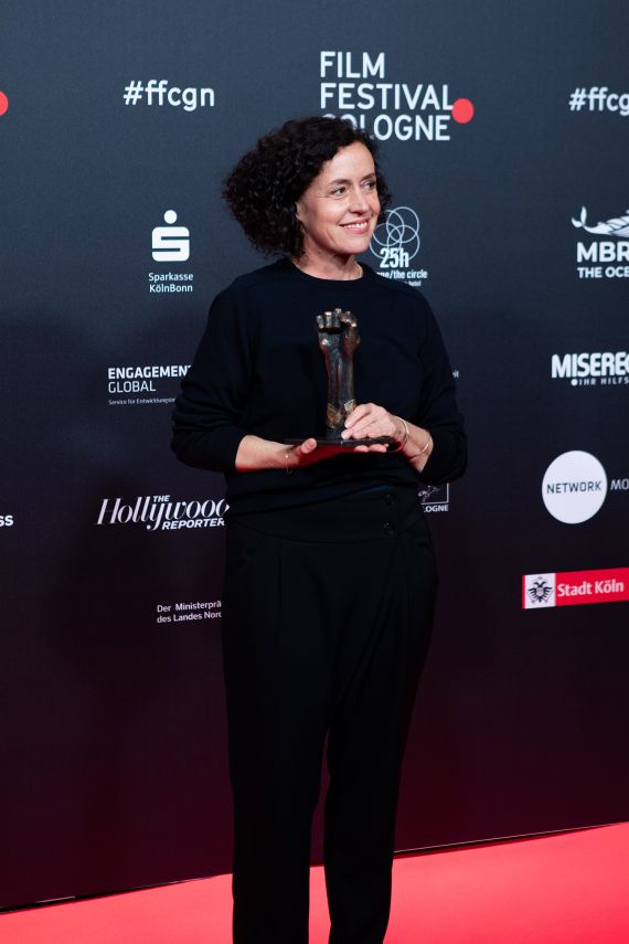 Die Schauspielerin vor einer Fotowand beim Filmfestival Cologne mit dem Manfred-Stelzer-Preis in der Hand.