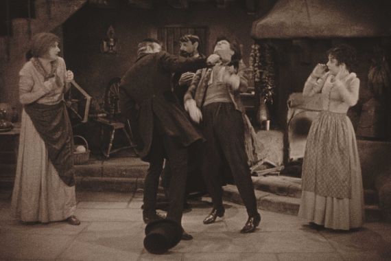 Zwei Männer prügeln sich theatralisch, während zwei Frauen erschrocken an der Seite stehen.