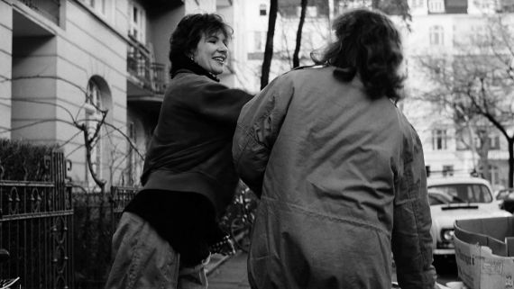 Eine lachende Frau ohrfeigt eine andere Person, die mit dem Rücken zur Kamera steht.