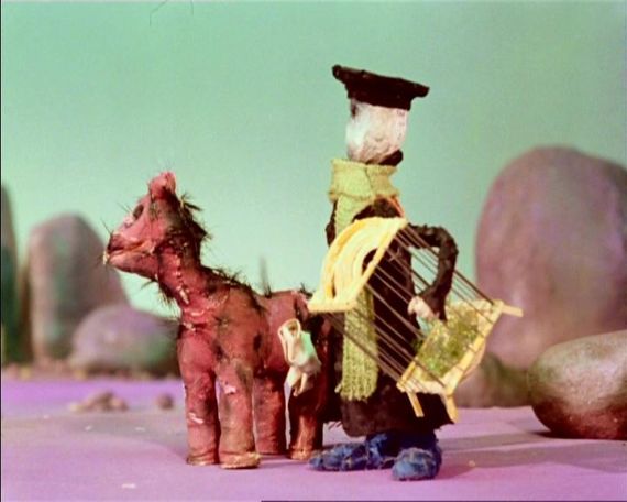 Szenenfoto aus einem Puppentrickfilm: Ein Mann mit einem leeren Vogelk&auml;fig neben einem Pferd.