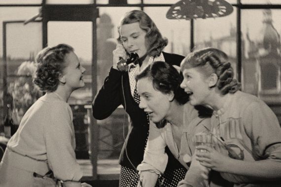 Vier Frauen, darunter Ingrid Bergman am Telefon, mit blonden und brünetten Haaren, amüsieren sich über etwas..