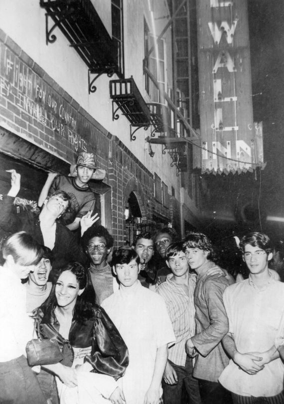 Eine Gruppe junger Menschen vor einem Geb&auml;ude mit einem beleuchteten Schild.