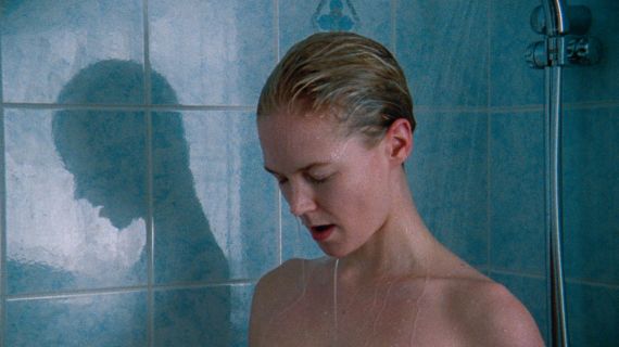 Eine Frau mit blonden Haaren steht unter der Dusche. Sie hat die Augen geschlossen und guckt nach unten. 