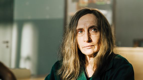 Eine Frau mit langem Haar, die nachdenklich aussieht. Sie wird von der Sonne beschienen.