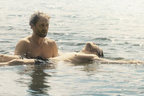 Zwei M&auml;nner sind im Wasser. Der Eine tr&auml;gt den Anderen, der auf dem R&uuml;cken liegt. 