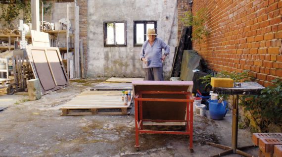 Eine alte Frau steht in einem Schuppen und arbeitet dort.