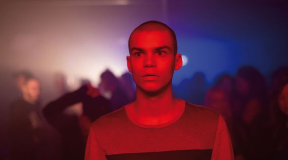 Ein Mann steht erschrocken mit offenem Mund in einem Club mit rotem Licht.