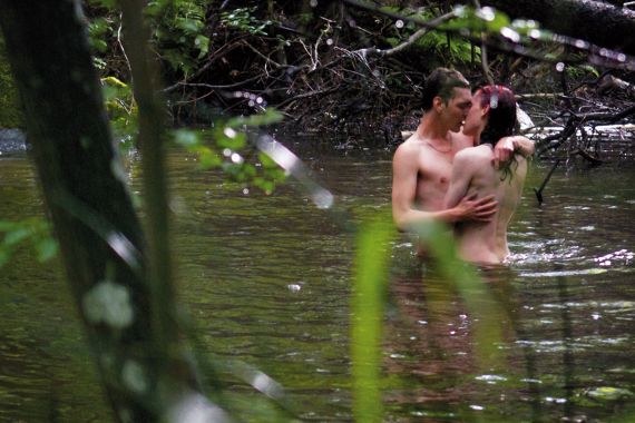 Zwei Personen stehen nackt in einem Fluss und k&uuml;ssen sich.